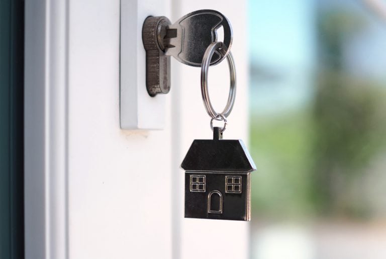 Close up of a young-ish woman with dark curly hair opening curtains to the right looking outside with a smile on her face