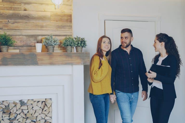 Couple looking at interior of home with real estate agent and backdrop of a white brick fireplace
