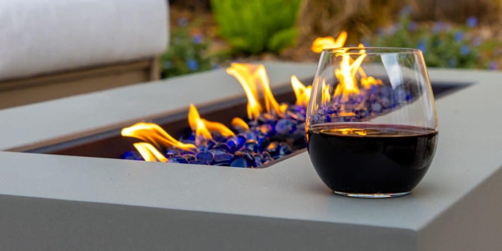 Glass of red wine on edge of firepit outdoors