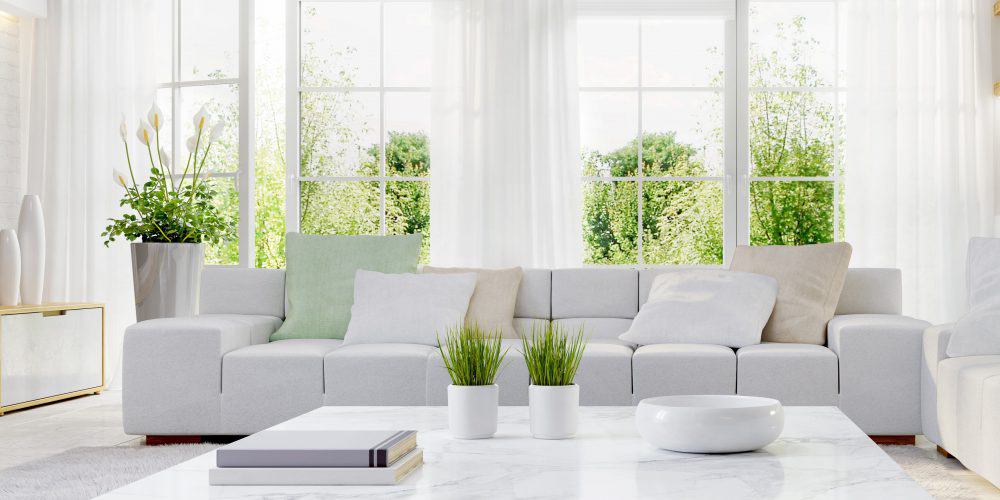 Modern great room with white walls and furniture and sliders showing lush greenery beyond