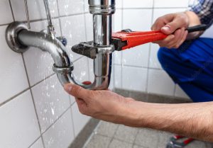 man fixing leaking pipe under sink