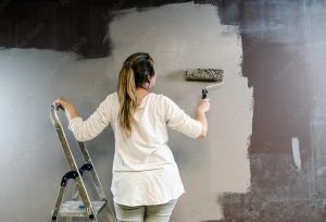 woman facing dark gray wall painting it a lighter gray