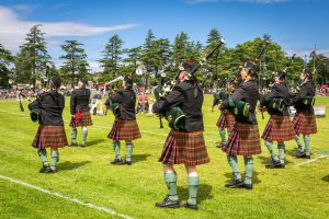 Men in kilts playing bagpipes outside in open area on sunny day