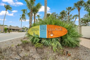 Surfboard sign stating Siesta Key Village with palms behind it