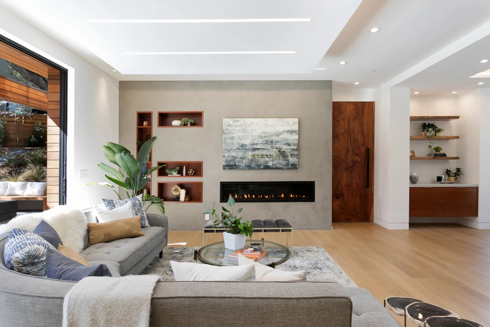 Contemporary living room with a linear fireplace, a concrete-look feature wall, and light oak floors