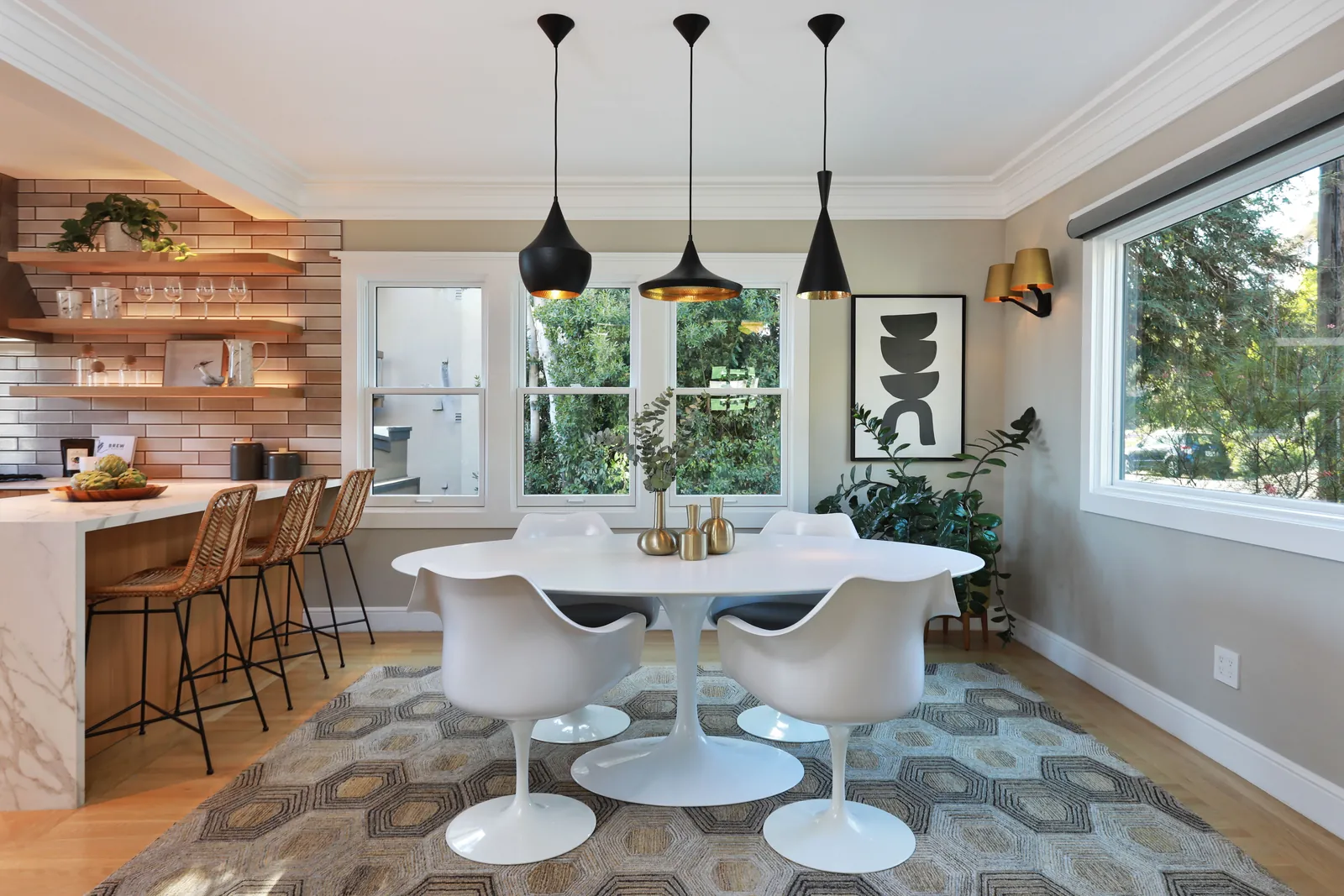 Updated dining area with a round white table beneath three black pendant lights and a brick-tile kitchen bar