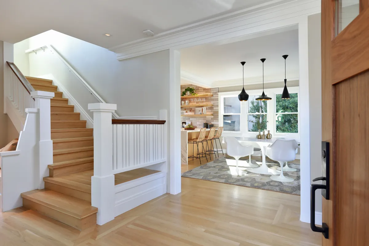 Home entry with a wood staircase opening toward a bright kitchen and dining area