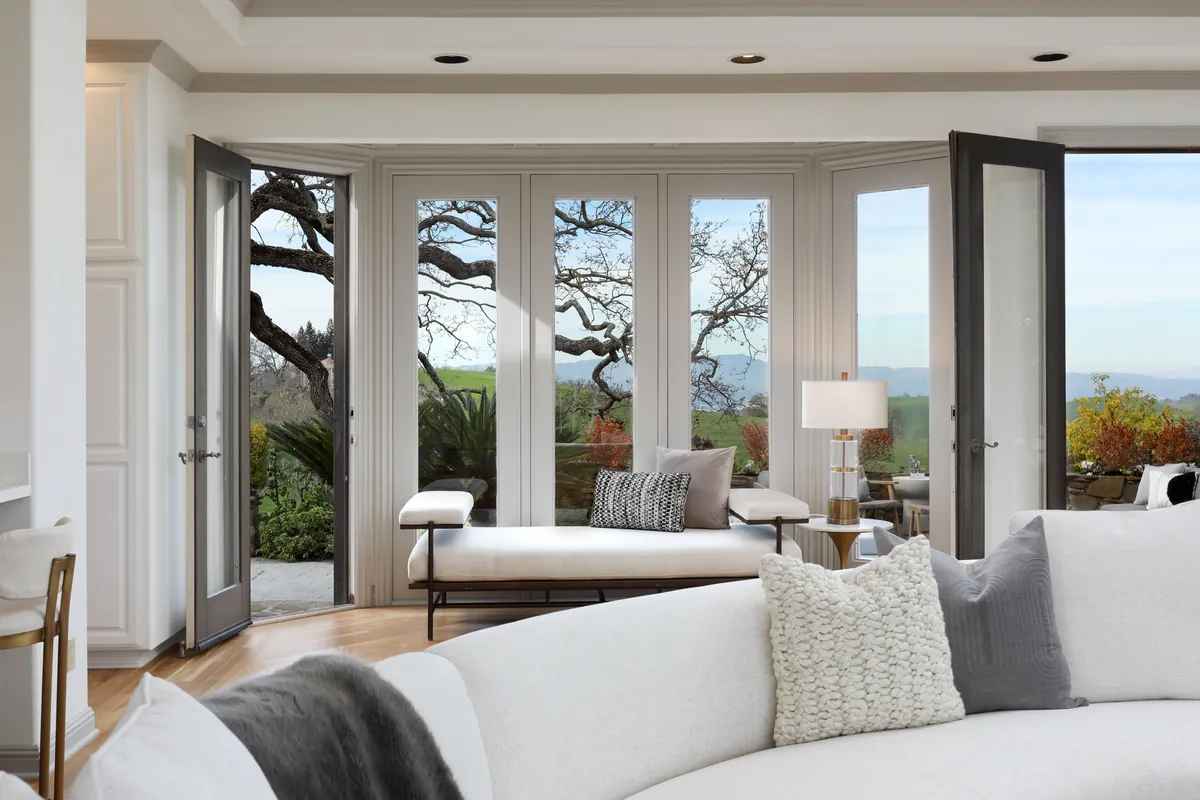 Living room with a wall of windows framing oak trees and distant East Bay hills