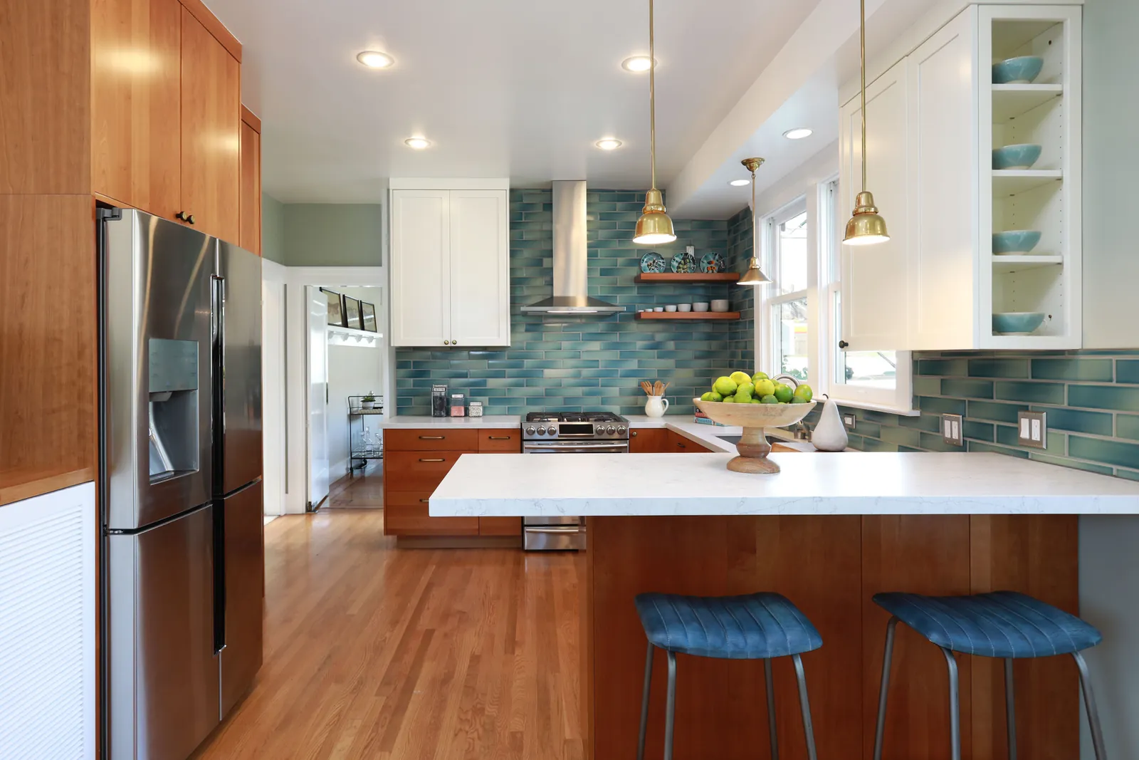 Renovated kitchen with wood cabinets, white countertops, blue-green tile backsplash, and brass pendant lights