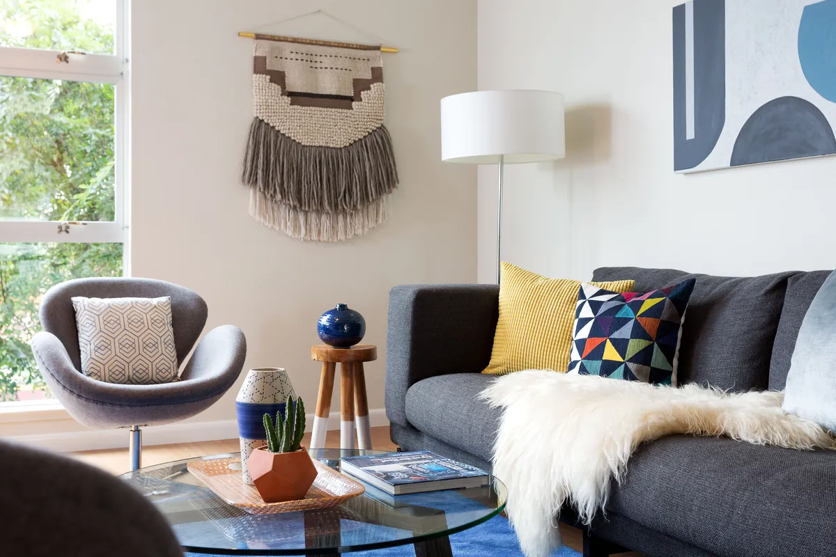 Staged living room with a gray sofa, accent pillows, and natural light from large windows