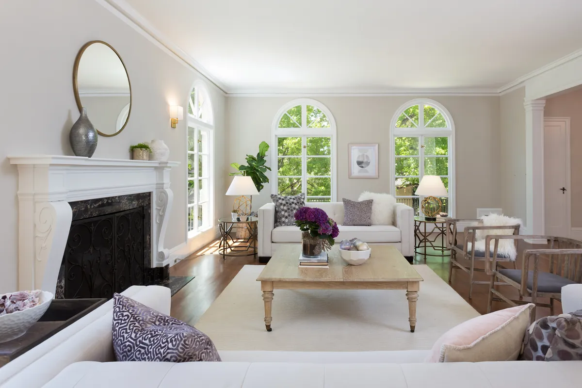 Traditional living room with arched windows, a carved mantel fireplace, and hardwood floors