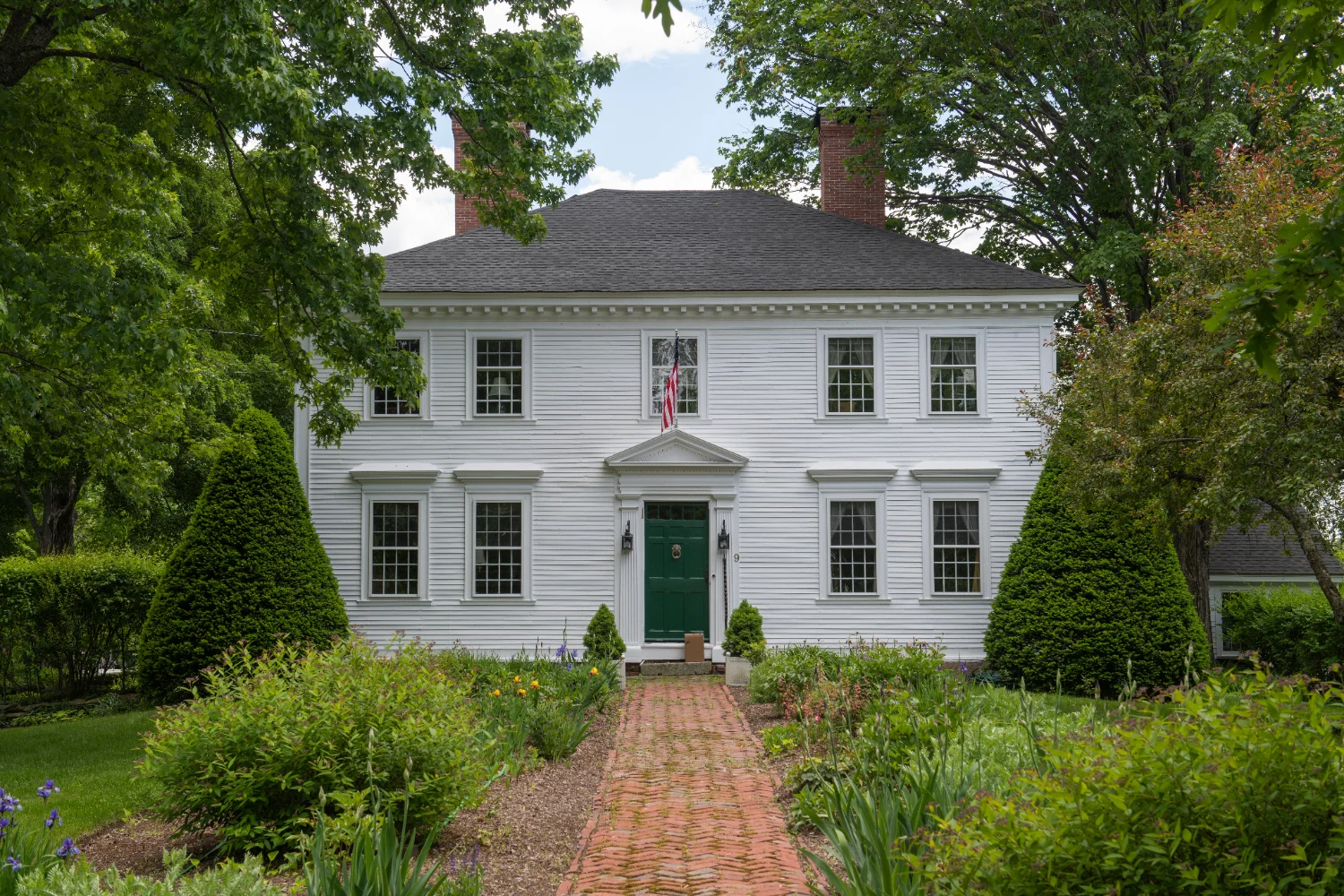White Federal-style colonial home with a green front door and a brick walkway