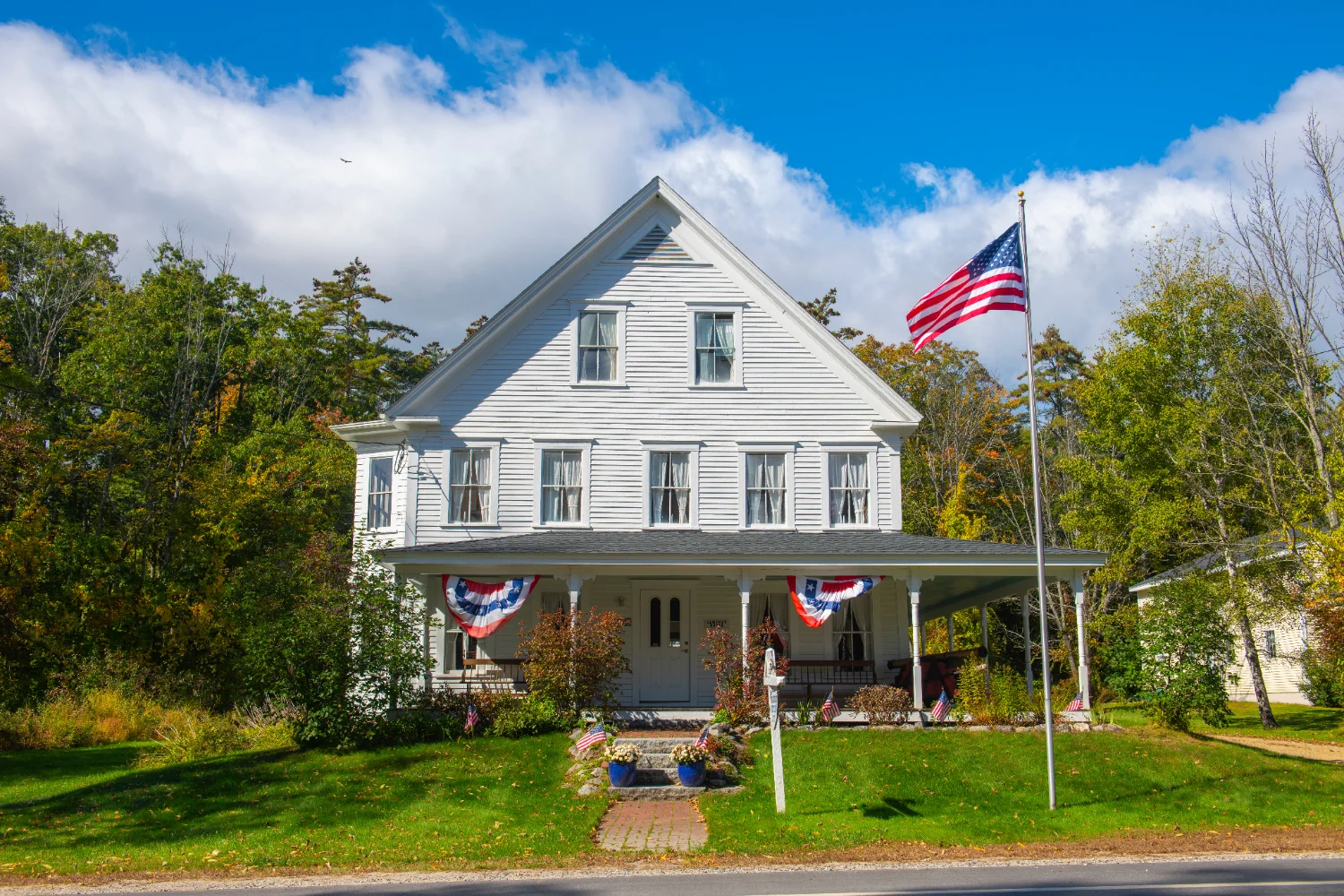 New Hampshire farmhouse with a wraparound porch, patriotic bunting and an American flag