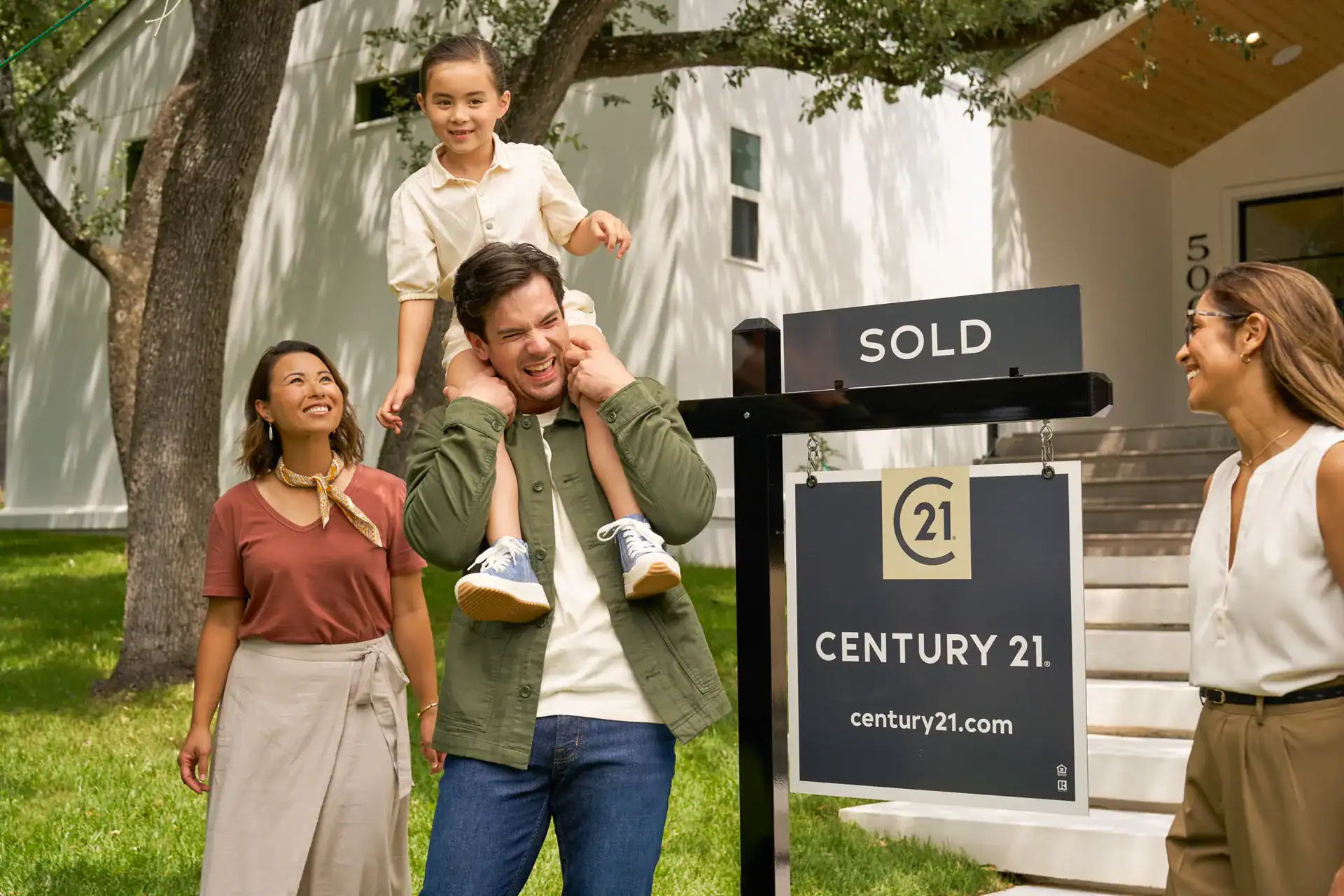 Century 21 agent with a family outside their home beside a SOLD sign