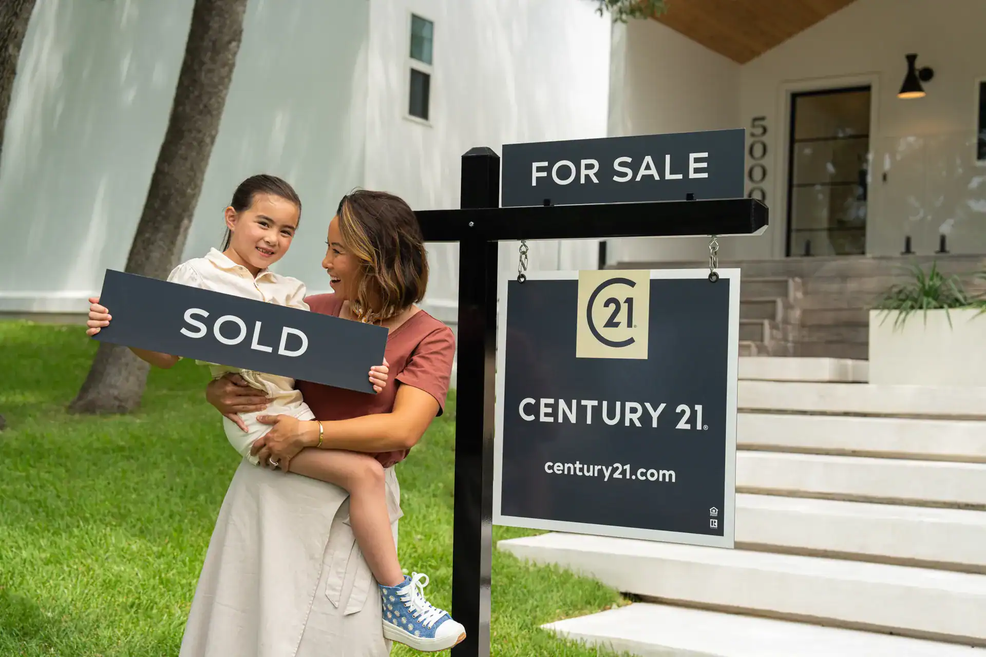 Mother and daughter holding a SOLD sign beside a Century 21 sign