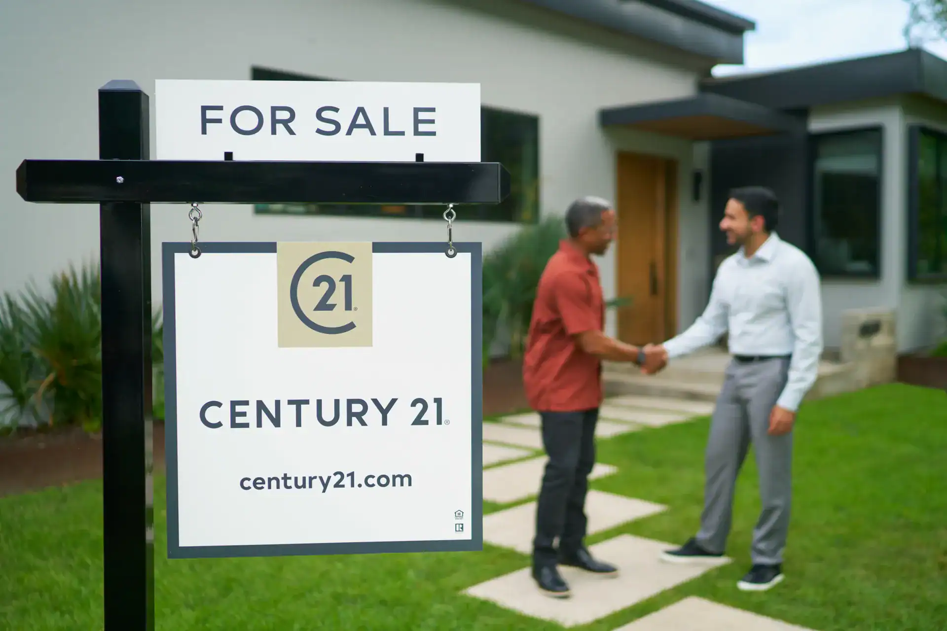 Two men shaking hands beside a Century 21 FOR SALE sign