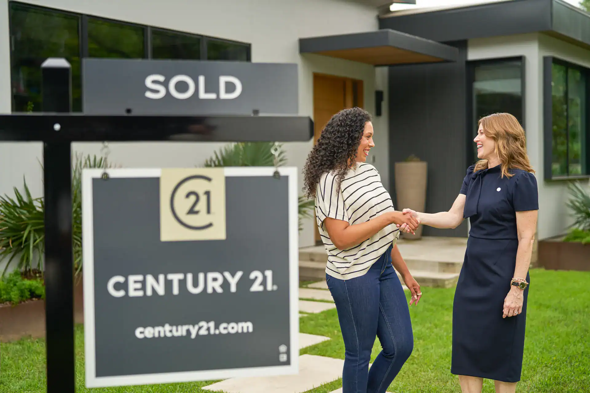 Two women shaking hands beside a Century 21 SOLD sign