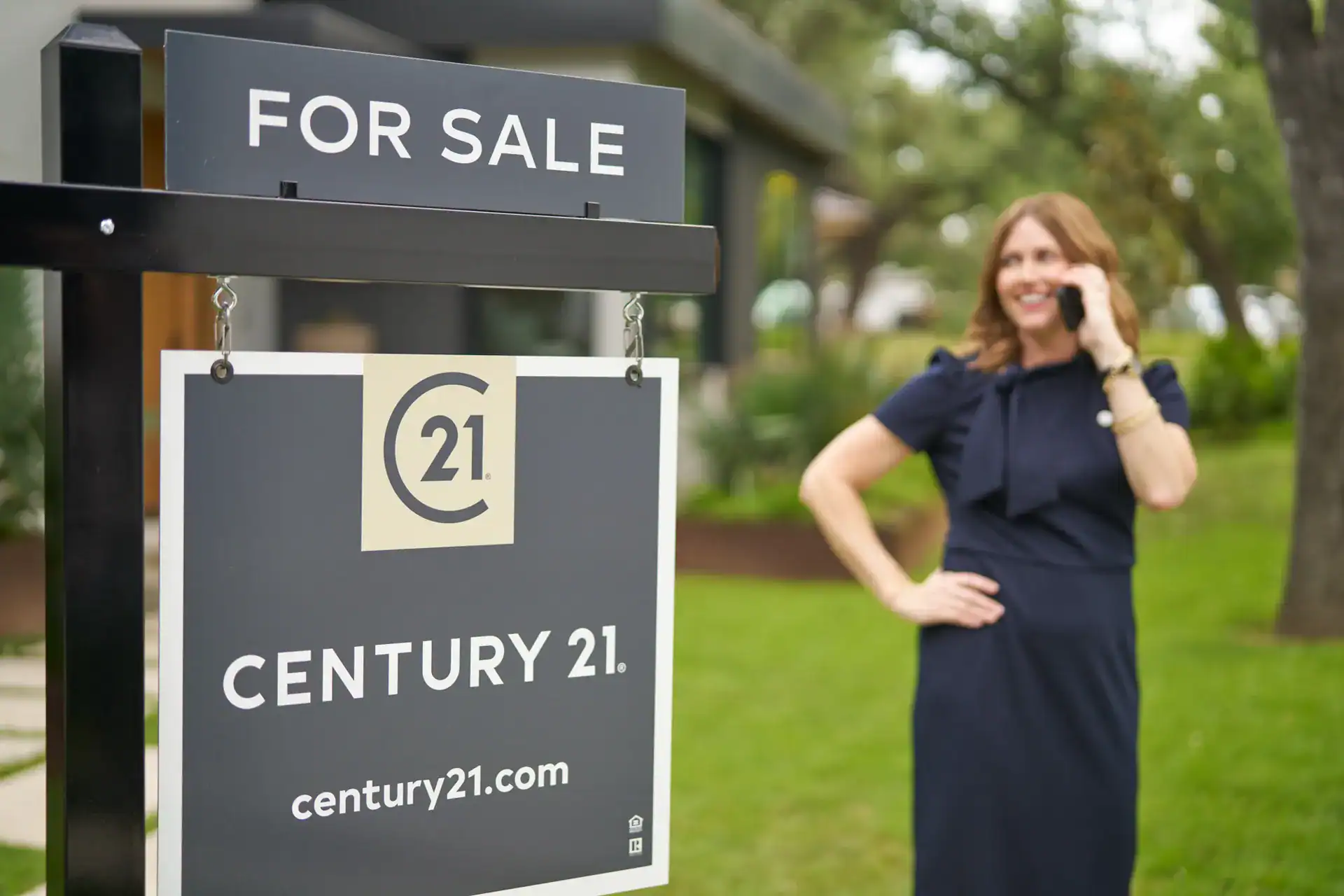 Century 21 agent on the phone beside a FOR SALE sign