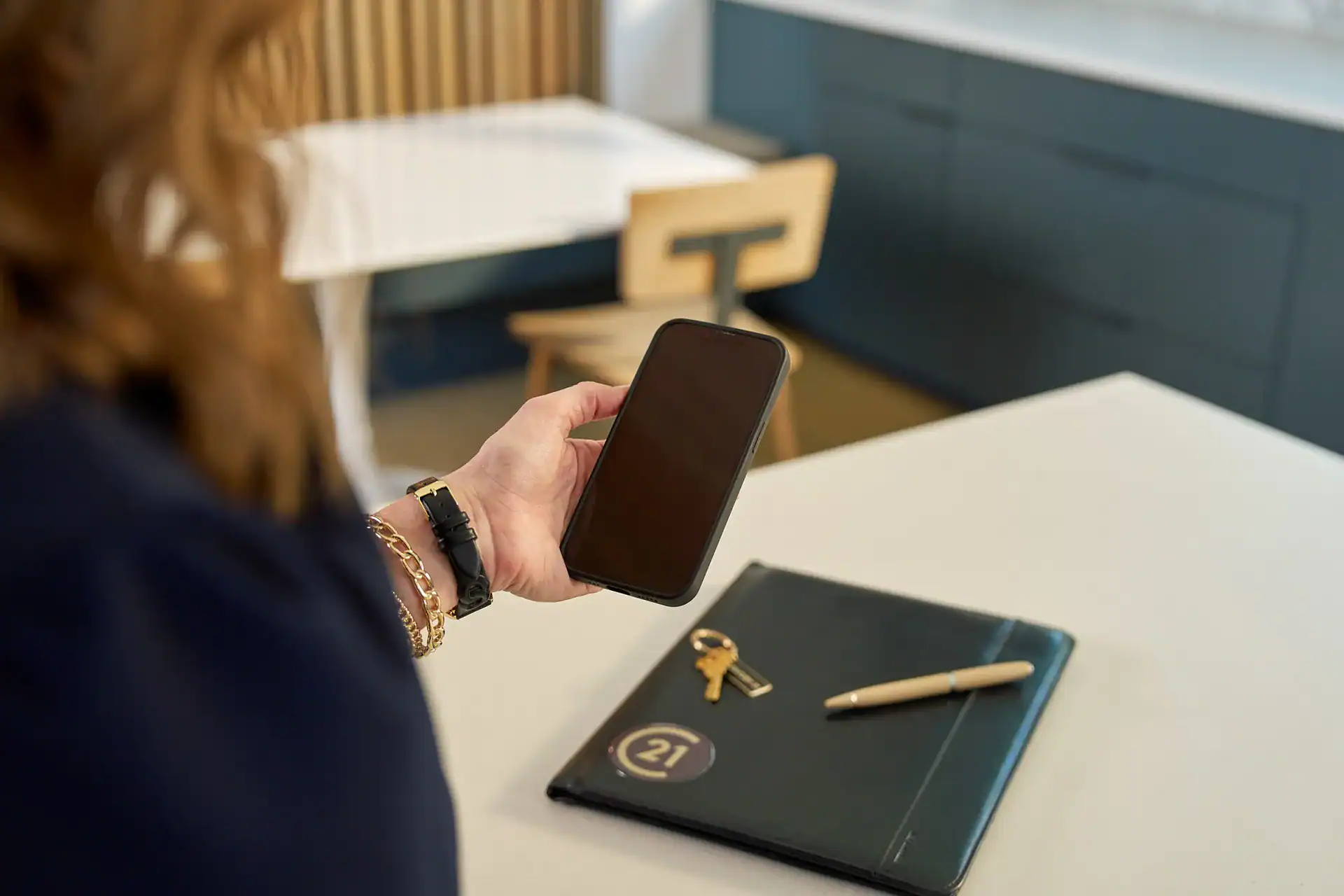 Agent holding a phone beside a Century 21 notebook and house keys