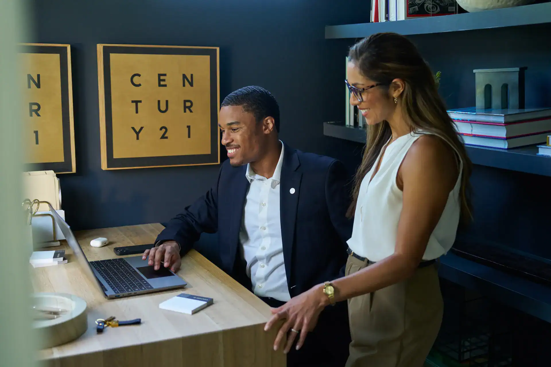 Two Century 21 agents reviewing work on a laptop