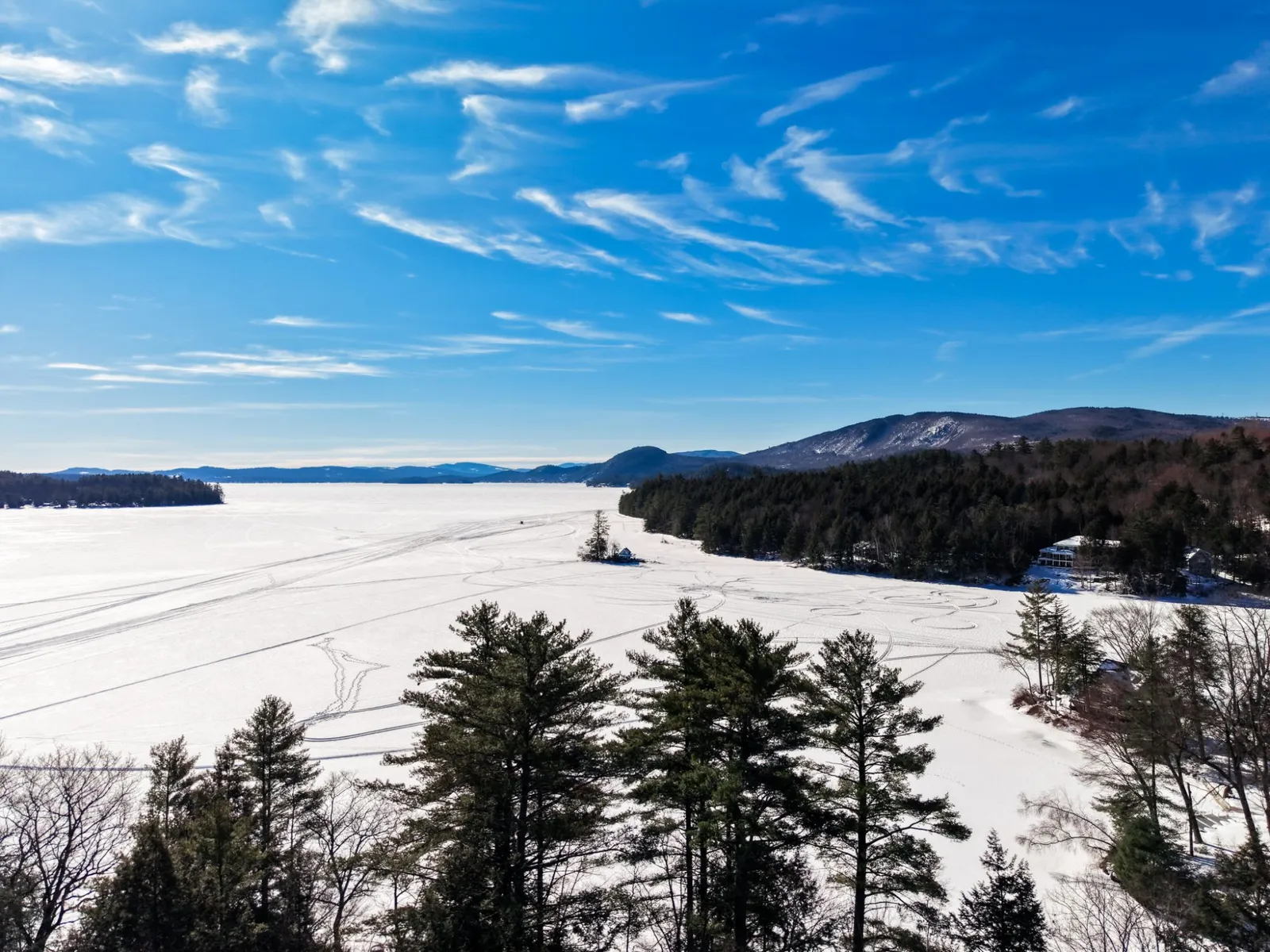 Aerial view of frozen, snow-covered Newfound Lake with tracks across the ice and the White Mountains beyond