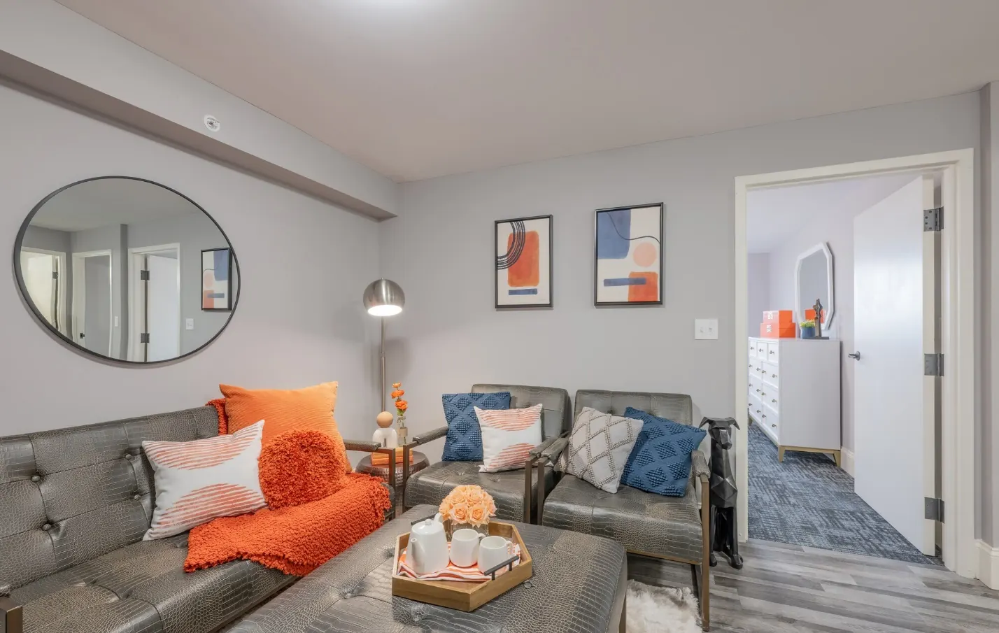 Living room at Huntington Exchange in Providence with a gray sofa, orange accent pillows and an open door to the bedroom