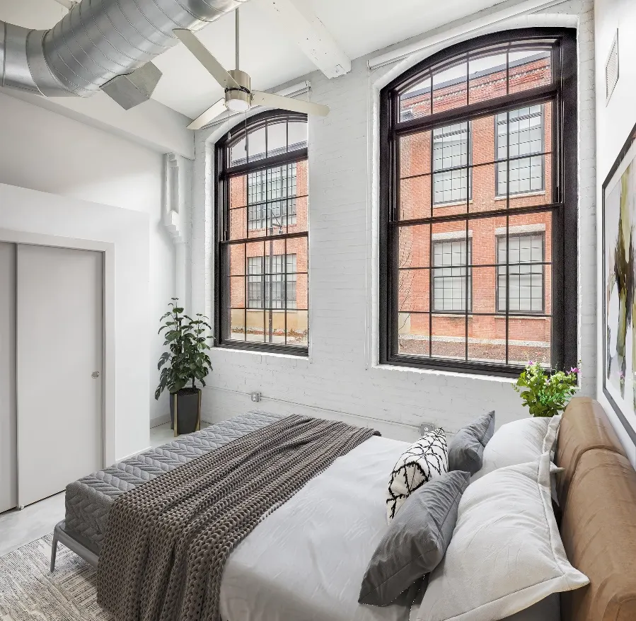 Bedroom at Paragon Mill Apartments in Providence with white-painted brick walls and tall black-framed mill windows