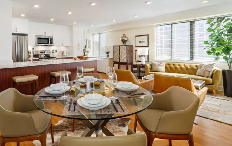 Dining table set for four at Regency Plaza, with orange lounge chairs and a stainless steel kitchen behind