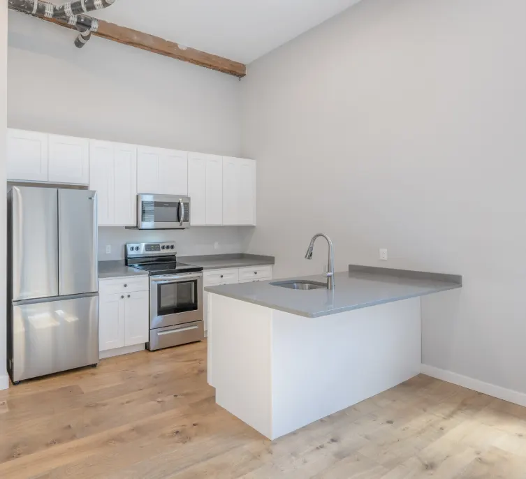 White kitchen at Strive Lofts with stainless steel appliances and a gray-topped island