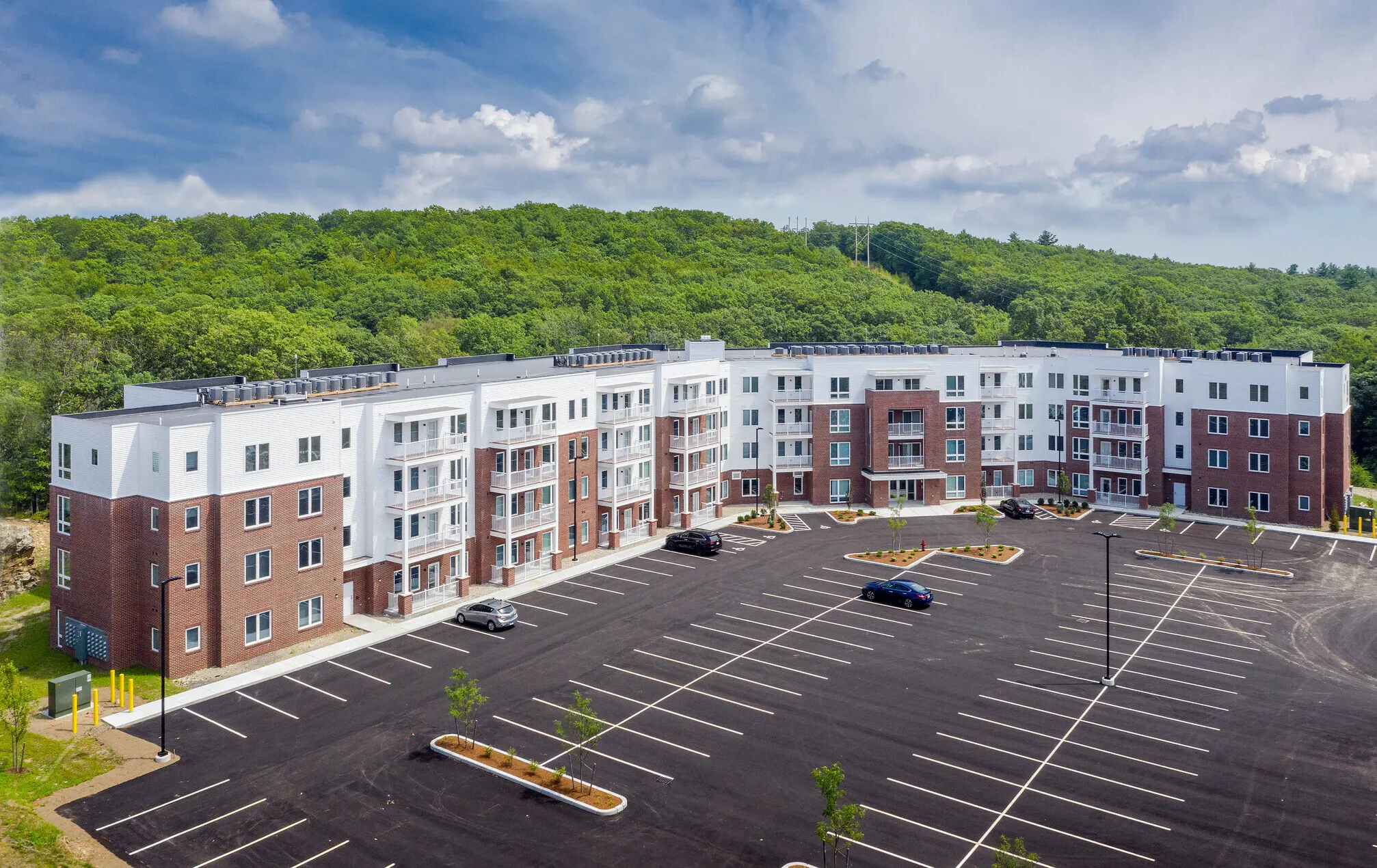 Aerial view of The Club at Dowling Village apartment buildings in North Smithfield, set against a wooded hillside