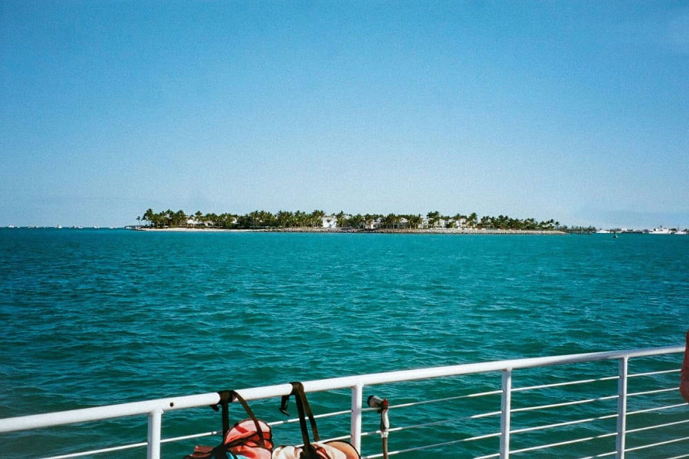  View from a boat over turquoise water, gazing toward a distant island lined with palm trees under a clear blue sky—an iconic Sandyport The Bahamas scene.