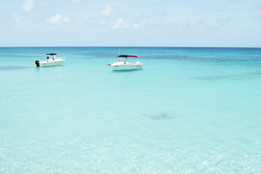 Two small white boats are anchored in calm, clear turquoise water under a partly cloudy sky near Sandyport, The Bahamas.