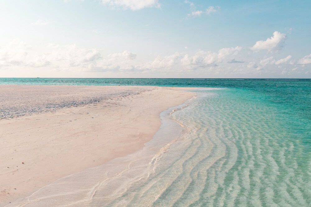  View from a boat over turquoise water, gazing toward a distant island lined with palm trees under a clear blue sky—an iconic Sandyport The Bahamas scene.