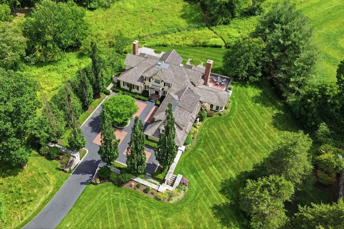 Aerial drone view of an estate home surrounded by trees and lawns