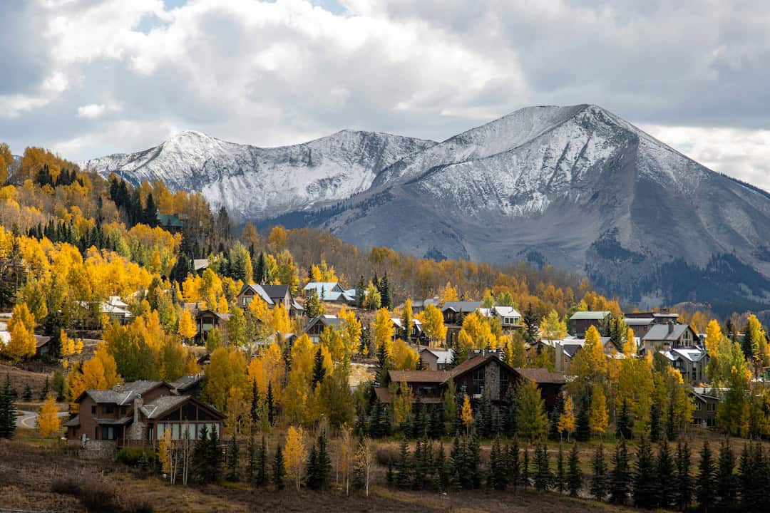 Homes tucked among golden aspens with a snow-capped peak above Crested Butte, Colorado