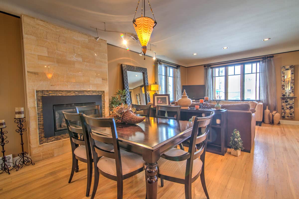 Dining table with extra chairs by a tiled fireplace in a gold-walled room before staging, Denver