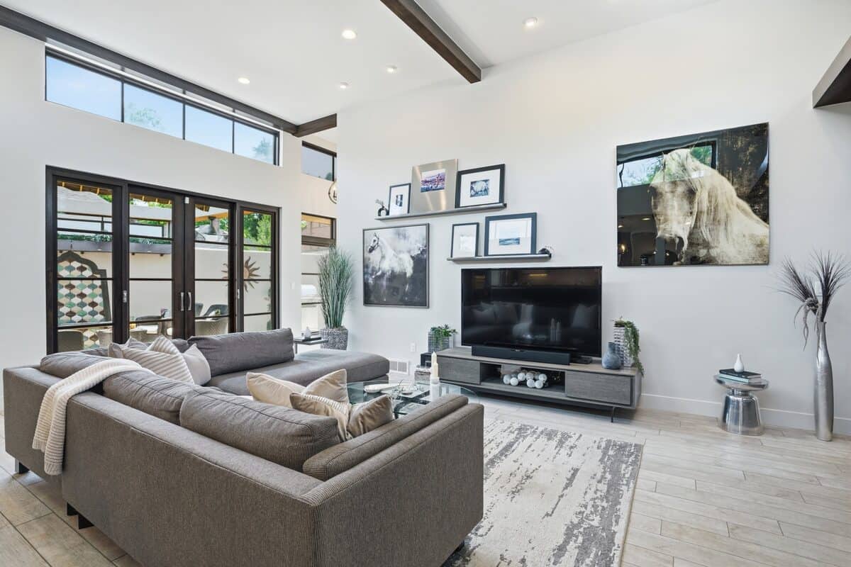 Great room with a gray sectional, neutral rug, and wood beams after staging, Denver