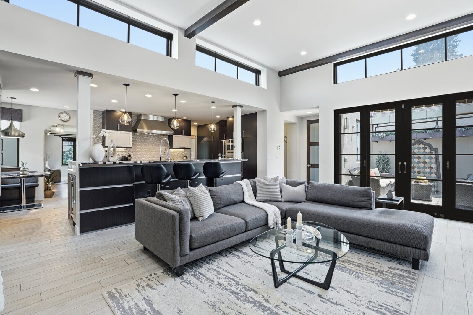 Open great room with a gray sectional, high clerestory windows, and a kitchen island with black stools, Denver