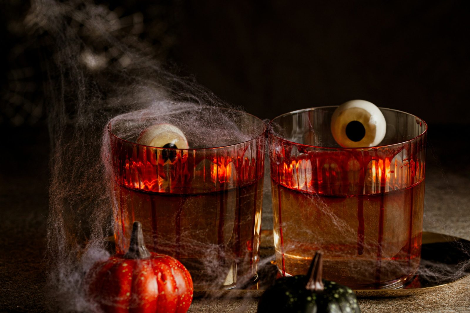 Two rocks glasses draped in cobwebs, rimmed with dripping fake blood and topped with candy eyeballs