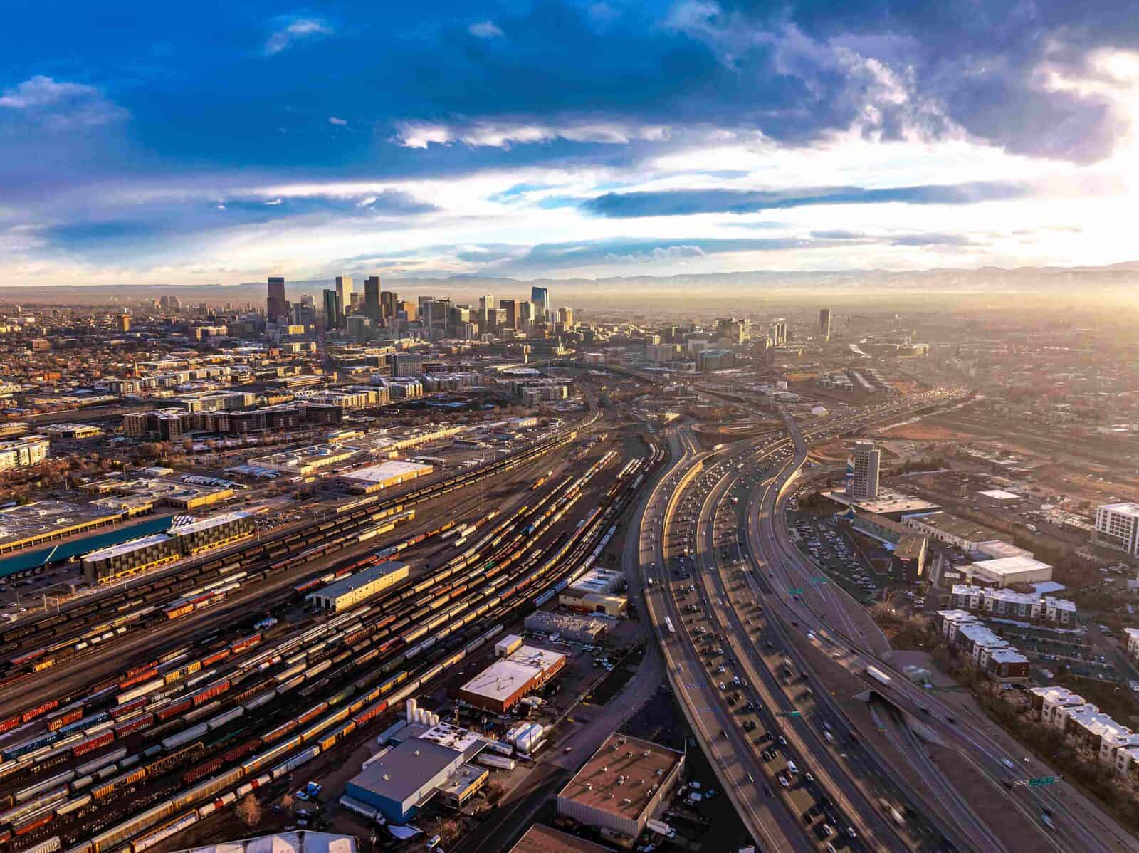 Downtown Denver skyline at sunset with a rail yard and highway in the foreground