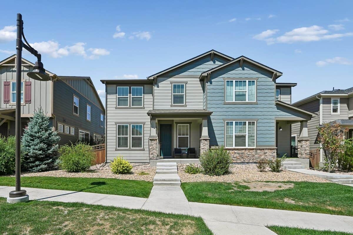 Two-story Centennial, Colorado home with sage green siding, stone accents, and a teal front door