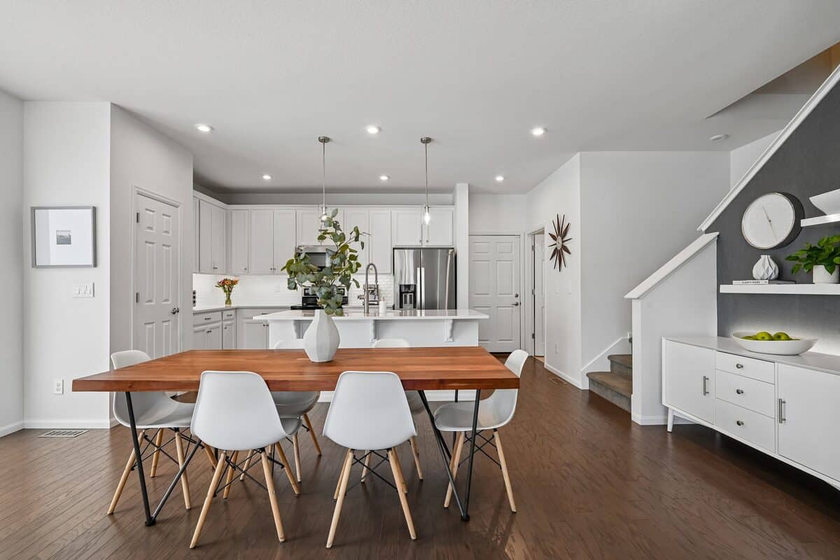 Open-concept kitchen and dining room with white cabinetry and a wood dining table, staged for showings