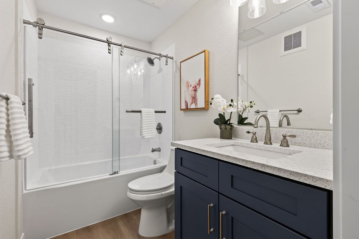 Bathroom with a blue vanity, quartz counter and glass-door tub at Hunters Chase