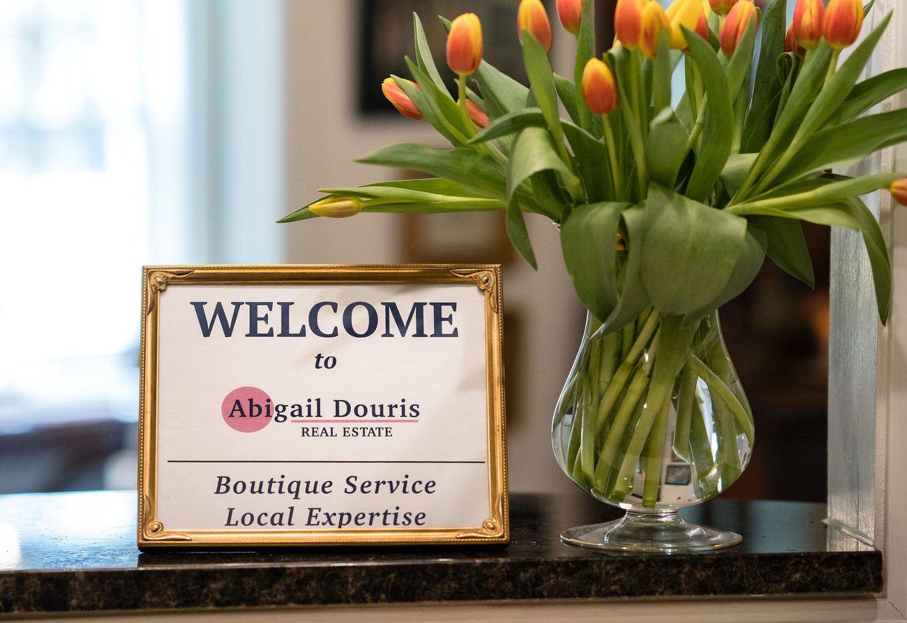Welcome sign on the front desk of the Abigail Douris Real Estate office, beside a vase of tulips